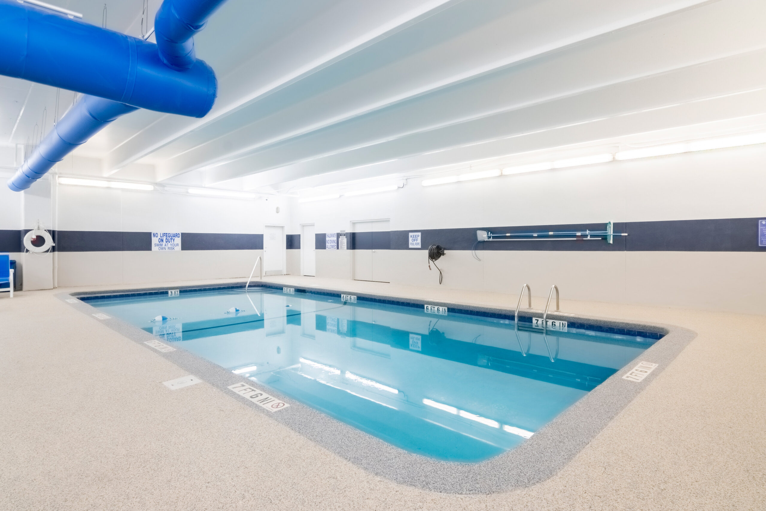 An indoor lap pool with a white and blue interior, surrounded by a gray floor and white walls.