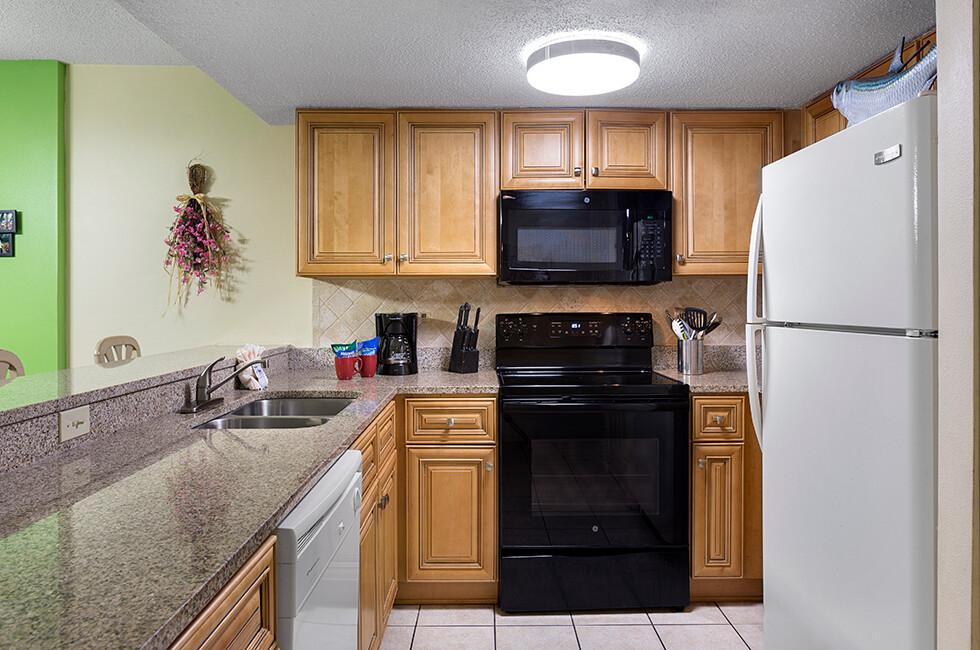 A kitchen with light wood cabinets, granite countertops, and black appliances.