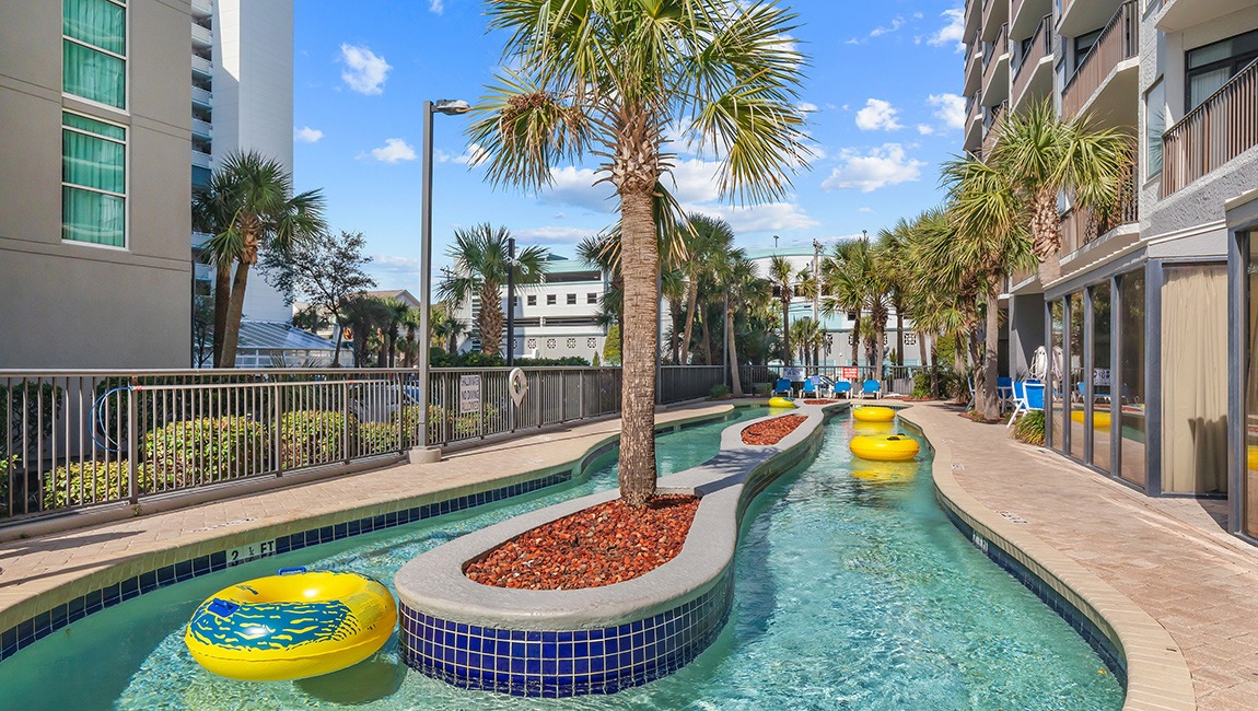 A winding pool with inflatable toys and palm trees in a tropical setting.