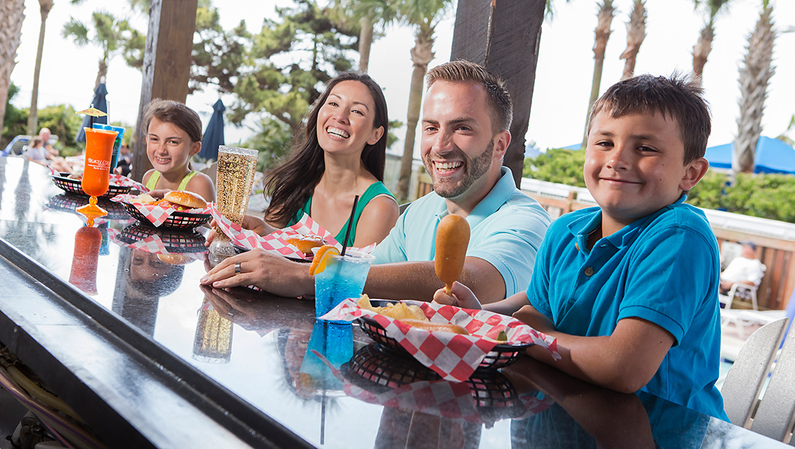 A family of four sitting at a bar with food and drinks